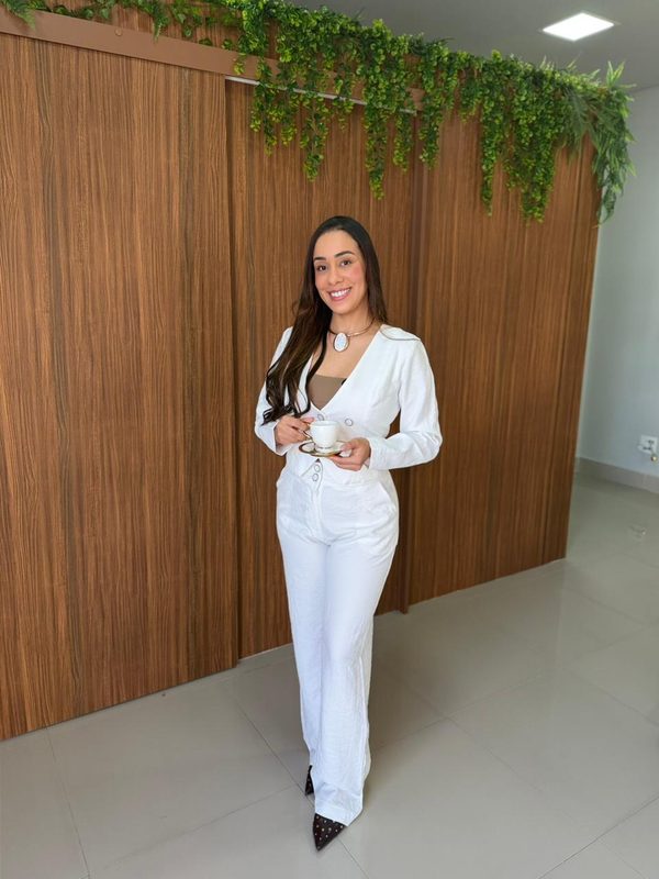 Dra. Joyce Menezes em pé no consultório, de branco.