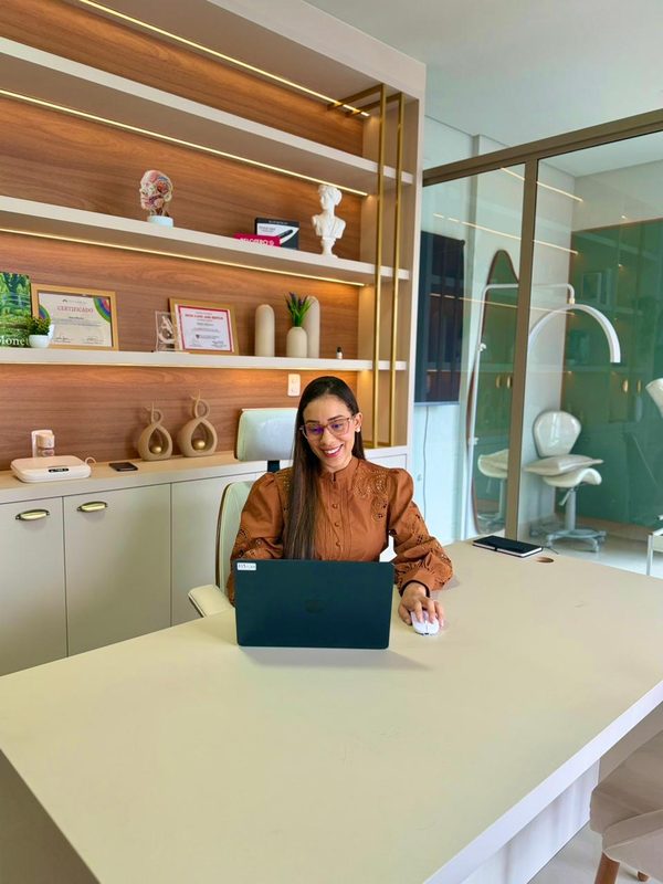 Dra. Joyce Menezes trabalhando no notebook do consultório.