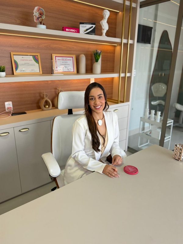 Dra. Joyce Menezes à mesa do consultório, de jaleco branco.